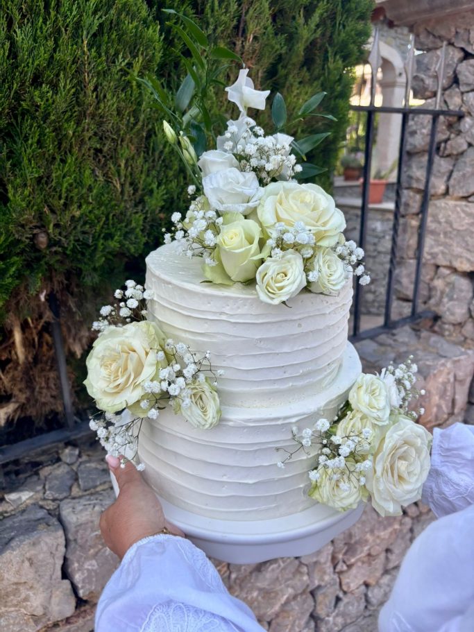 Hochzeitstorte Zweistöckige Torte dekoriert mit weißen Blumen und Efeu, auf einem Teller serviert.
