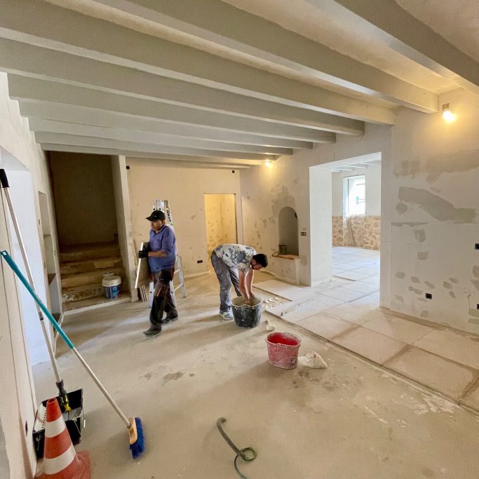 Platten verlegen Zwei Handwerker arbeiten in einem frisch renovierten Raum mit Holzdecke und Werkzeugen.