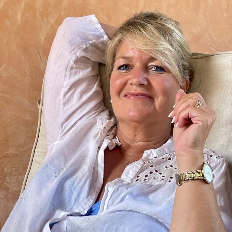 Anja Prömpeler Konditorin Konditorei - dulce de Anja Mallorca Frau mit blonden Haaren sitzt entspannt auf einem Sofa und lächelt. Anja Prömpeler - Dulce de Anja Mallorca -