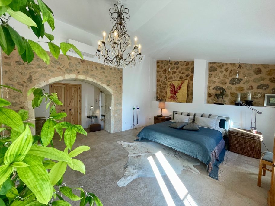 Homeservice Helles Schlafzimmer mit Steinwänden, einem großen Bett und einem Kronleuchter.