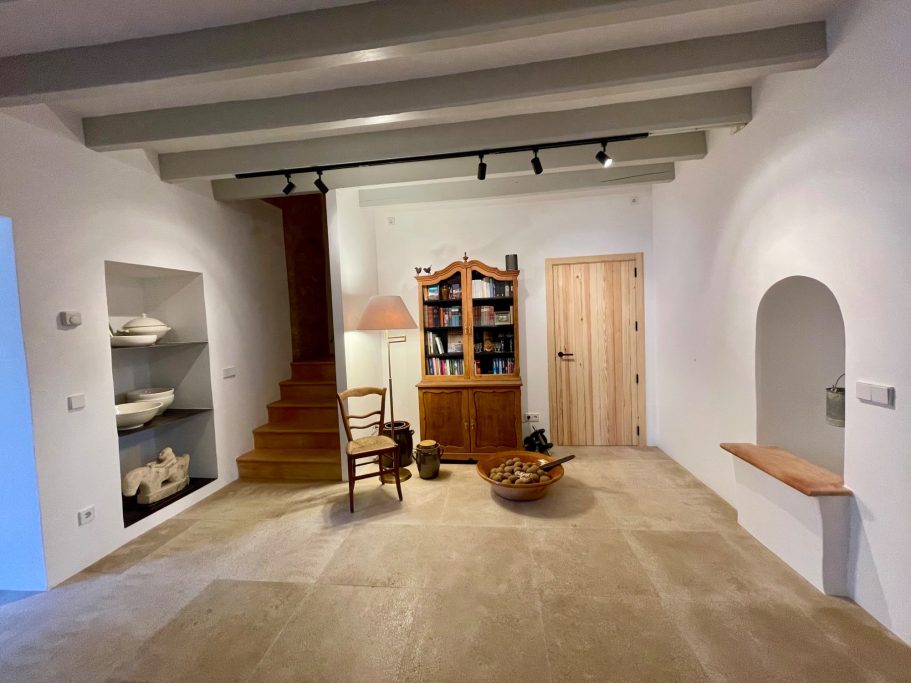 Objektbetreuung Heller Raum mit Holztreppe, Bücherregal, Stuhl und dekorativer Schüssel.