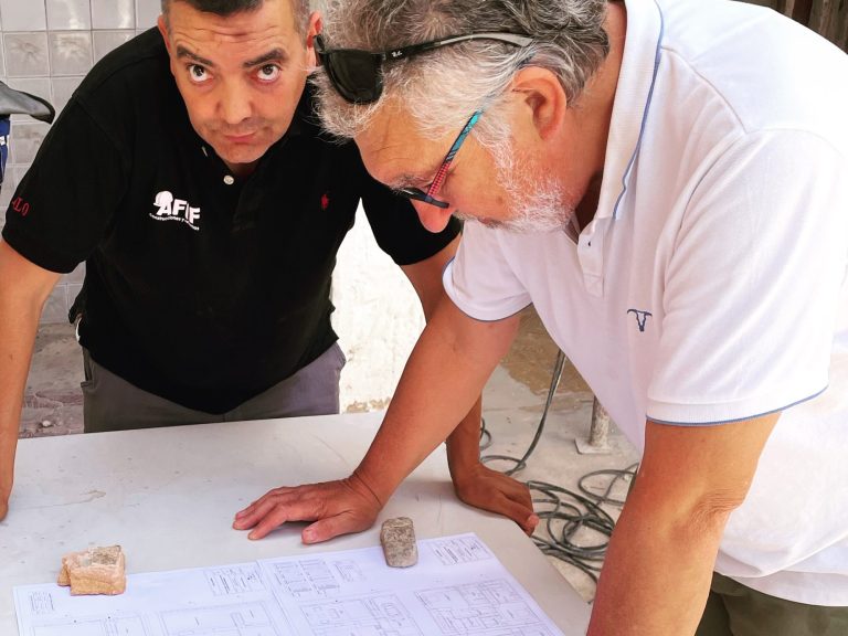 Zwei Männer analysieren Baupläne und Materialien an einem Tisch im Freien. Baubegleitung als Schnittstelle auf Mallorca