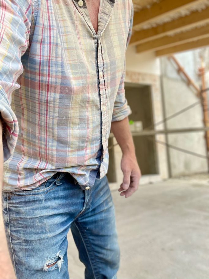 Baubegleitung Mann in kariertem Hemd und Jeans steht in einem Baustellenbereich.