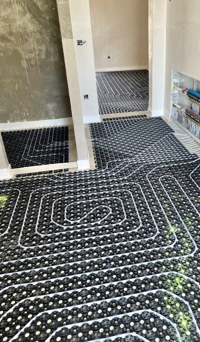 Baubegleitung Boden mit schwarzen und weißen Heizschlangen in einem unfertigen Raum.