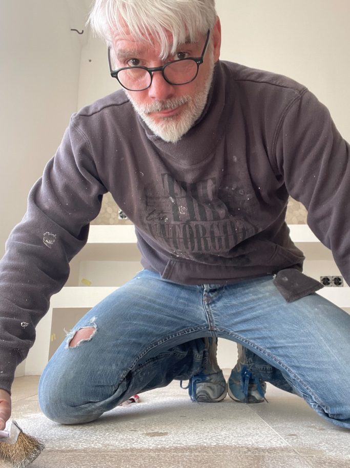 Fugenreinigung Ein Mann kniet auf dem Boden und arbeitet an einem Renovierungsprojekt.