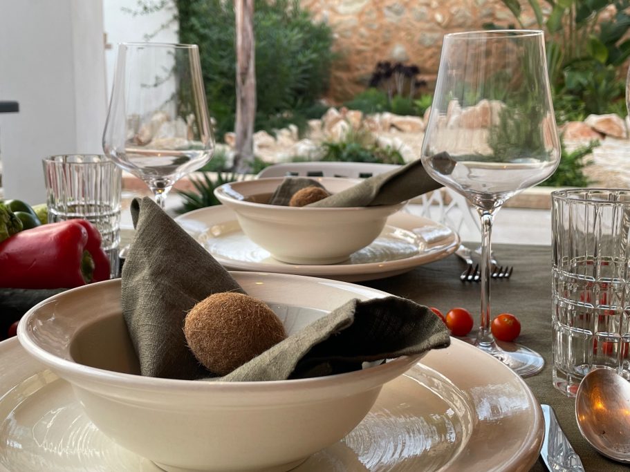 Ferienvermietung Elegant gedeckter Tisch mit Tellern, Gläsern und frischen Zutaten im Hintergrund.