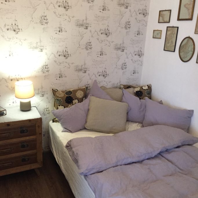 Ferienvermietung Gemütliches Schlafzimmer mit Bett, Kissen, Nachttisch und nostalgischen Wandbildern.