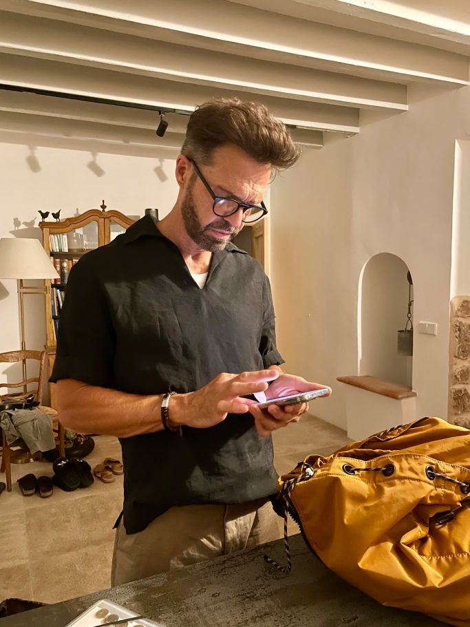Gerd - Termine Termine Mann mit kurzen Haaren und Brille, der auf ein Smartphone schaut, neben einer Tasche.