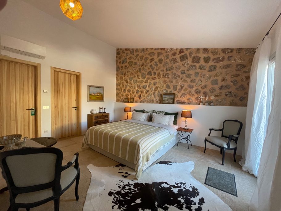 Ferienvermietung Schlafzimmer mit Steinwand, Doppelbett, zwei Stühlen und Holztüren.