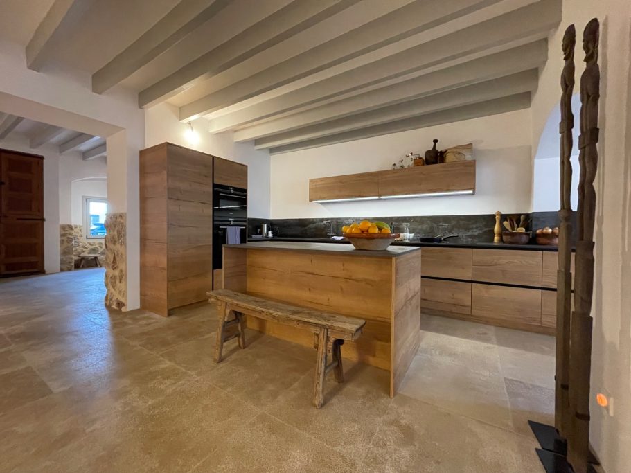 Objektbetreuung / Homeservice Moderne Küche mit Holzregal, Arbeitsfläche und Sitzgelegenheit in einem offenen Raum.