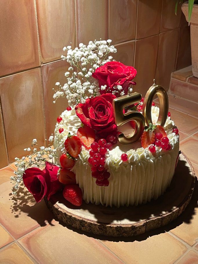 Zum 50. Hochzeitstag Torte zum 50. Jubiläum, dekoriert mit roten Rosen, Obst und weißen Blumen.