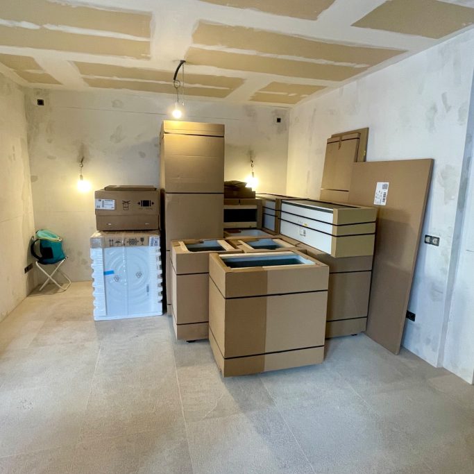 Objektbetreuung Ein Raum mit Stapeln von Kartons und Möbeln in einer leeren, ungefertigten Umgebung.