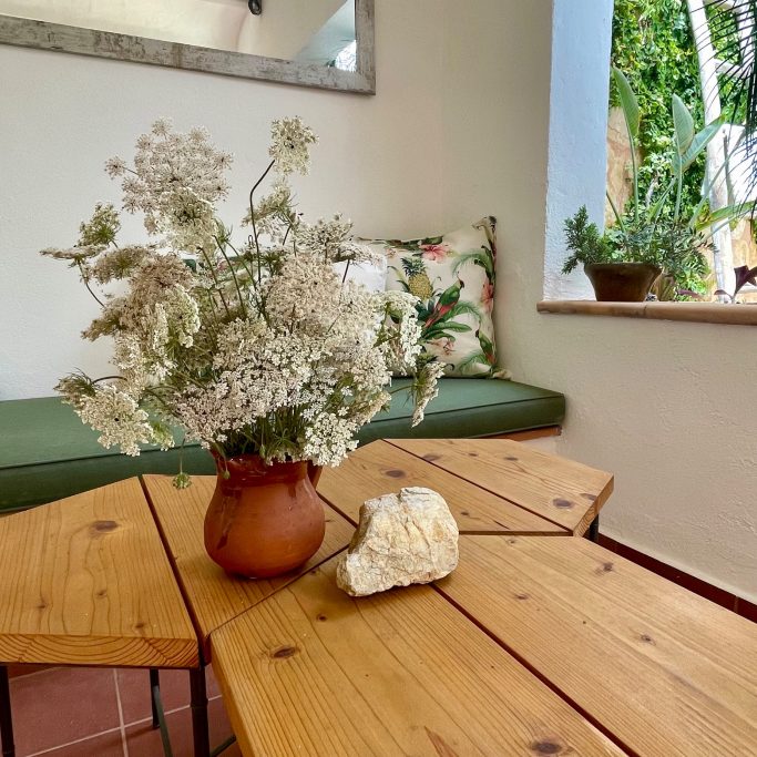 Objektbetreuung Blumenstrauß in einer Vase auf einem Holztisch, umgeben von Pflanzen und einem Sofa.