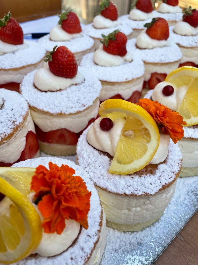 Törtchen für Ihr Event Mehrere luftige Törtchen mit frischen Erdbeeren, Zitronenscheiben und essbaren Blumen.