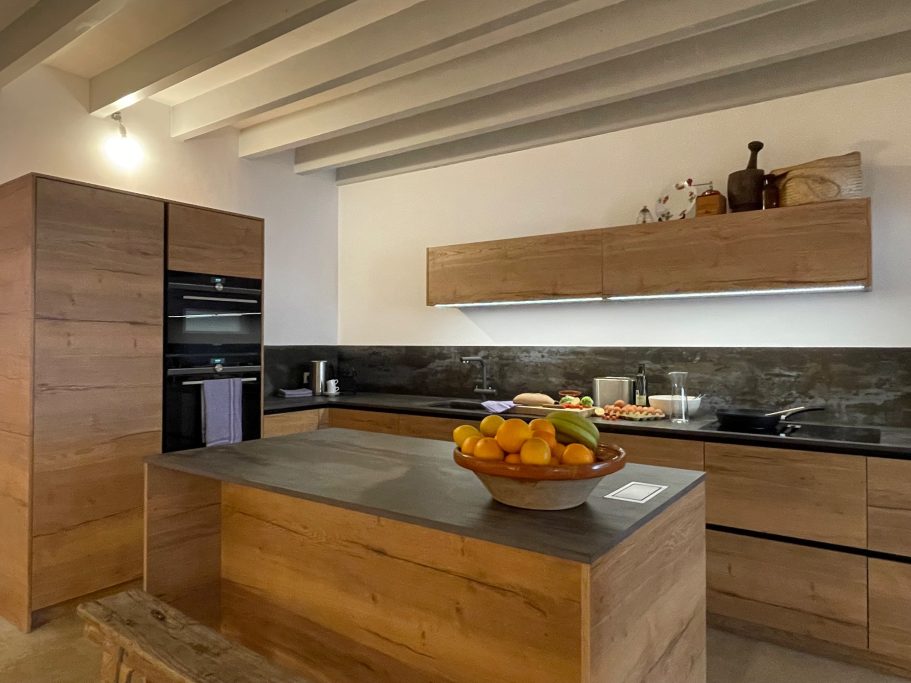 Homeservice Moderne Küche mit Holzmöbeln, einem Obstkorb und minimalistischer Ausstattung.