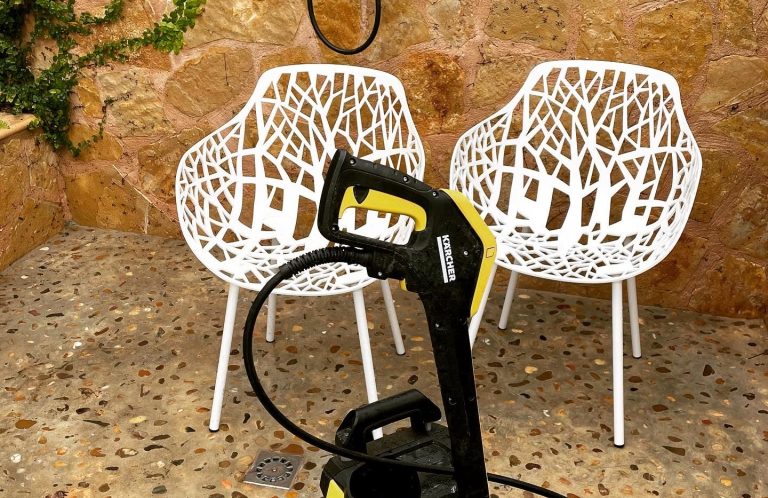 Zwei weiße, moderne Stühle vor einem rustikalen, steinernen Hintergrund und einem Hochdruckreiniger. Pflege von Terrassen  Mallorca