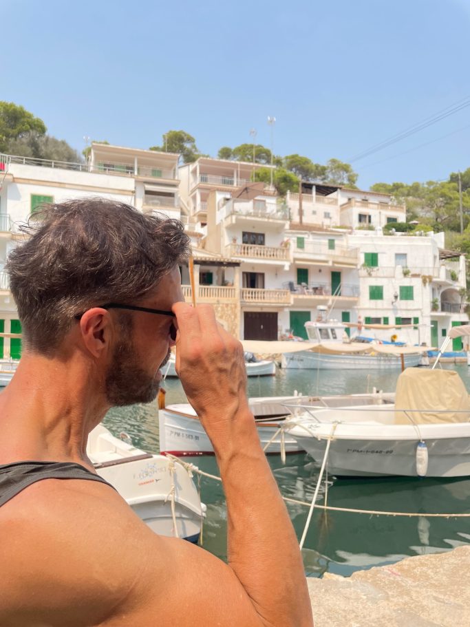 Klientenbesuch Mann mit Sonnenbrille, der an einem Hafen mit Booten und Häusern vorbeigeht.