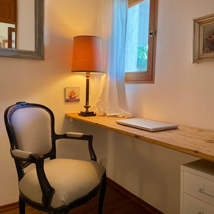 Homeservice Ein helles Zimmer mit einem Schreibtisch, einem Stuhl, einer Lampe und einem Fenster.