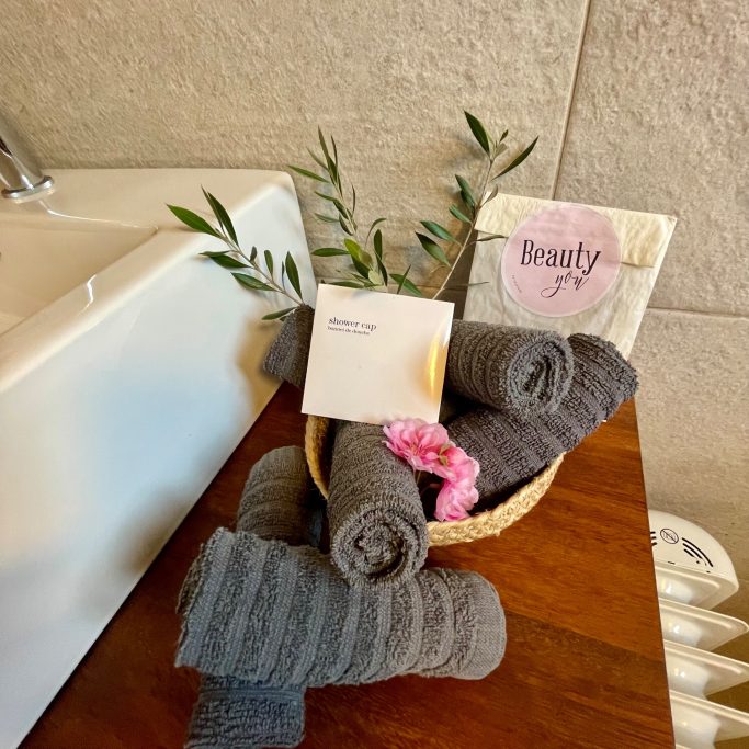 Ferienvermietung Graue Handtücher, eine Seife und Pflanzen in einem Korb auf einer Badezimmerablage.