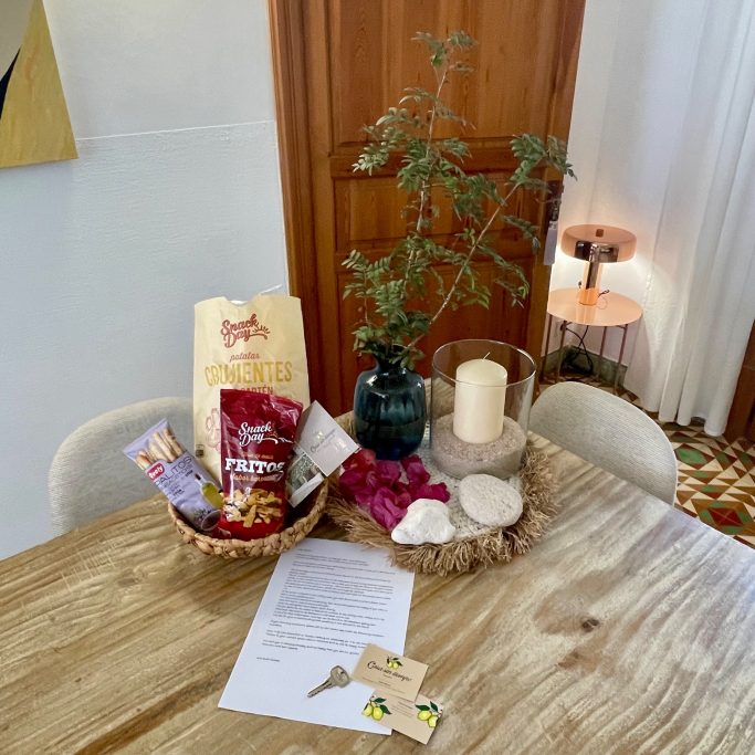 Ferienvermietung Ein dekorierter Tisch mit Snacks, einer Kerze, einer Vase und Pflanzen.