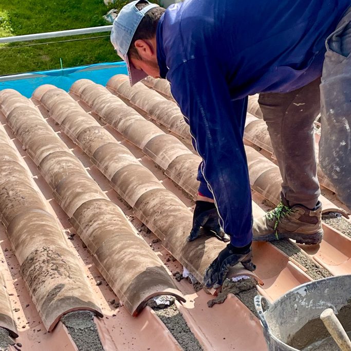 Dachsanierung Dachdecker verlegt Terrakottaziegel auf einem Dach.