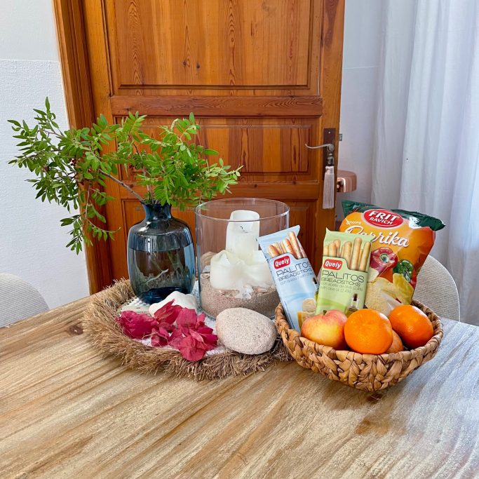 Ferienvermietung Ein dekorativer Tisch mit einer Vase, Obst, Snacks und frischen Kräutern.