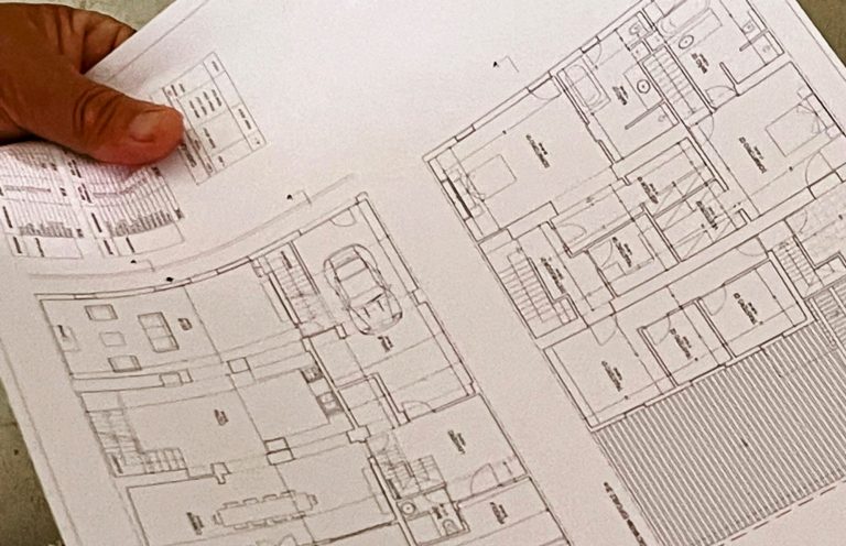 Hand hält einen Bauplan und Grundriss mit mehreren Räumen. Baubegleitung bei Sanierung und Renovierung auf Mallorca. 
