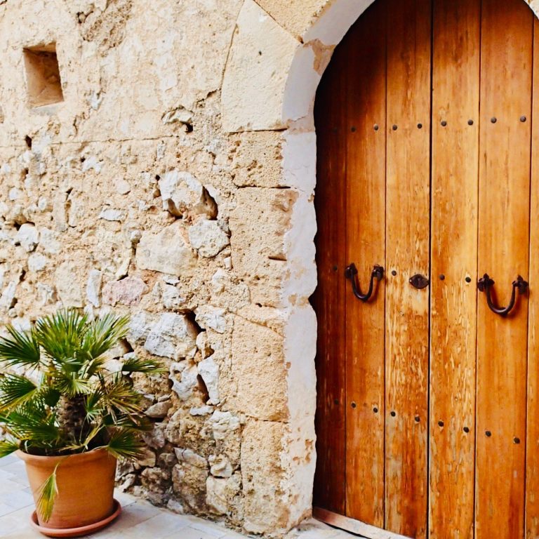 Holztür in einer steinernen Wand, daneben ein Blumentopf. Als Symbol für ein Komfort Sicherheitspaket im  Homeservice Mallorca