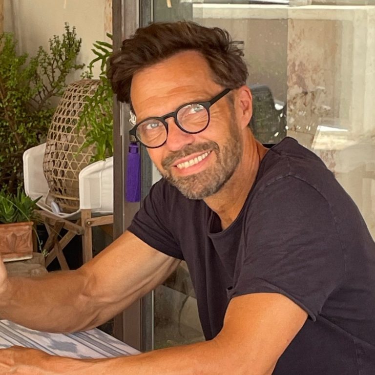 Gerd Lauterbach Homeservice Hausbetreuung Mallorca Mann mit Brille lächelt am Tisch, umgeben von Pflanzen und einem modernen Ambiente. Gerd Lauterbach Homeservice Mallorca