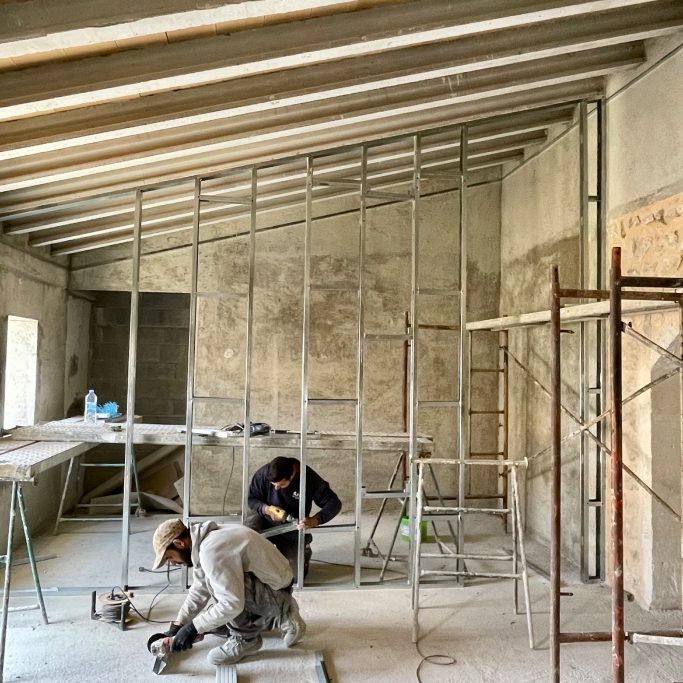 Trockenbau Zwei Handwerker arbeiten an einem Rohbau mit Stahlgerüsten und ungefertigten Wänden.