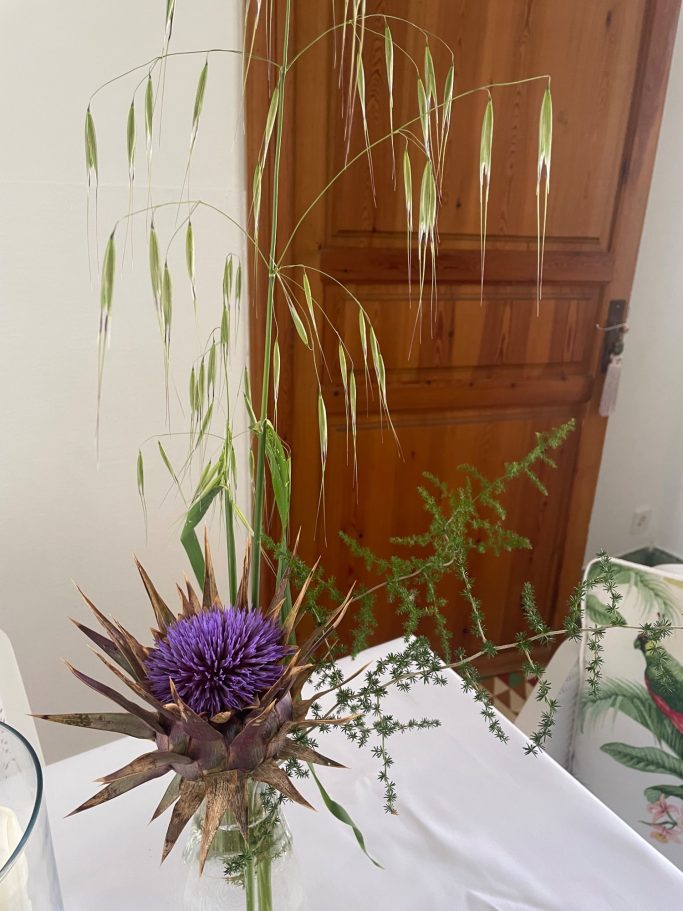 Ferienvermietung Bunte Blüten und Gräser in einer Vase, mit lila und grünen Elementen.