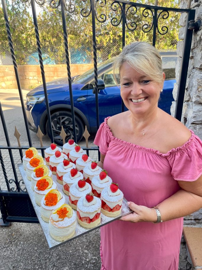 Törtchen für Ihr Event Eine Frau in einem rosa Kleid hält ein Tablett mit bunten Desserts vor einem Tor.